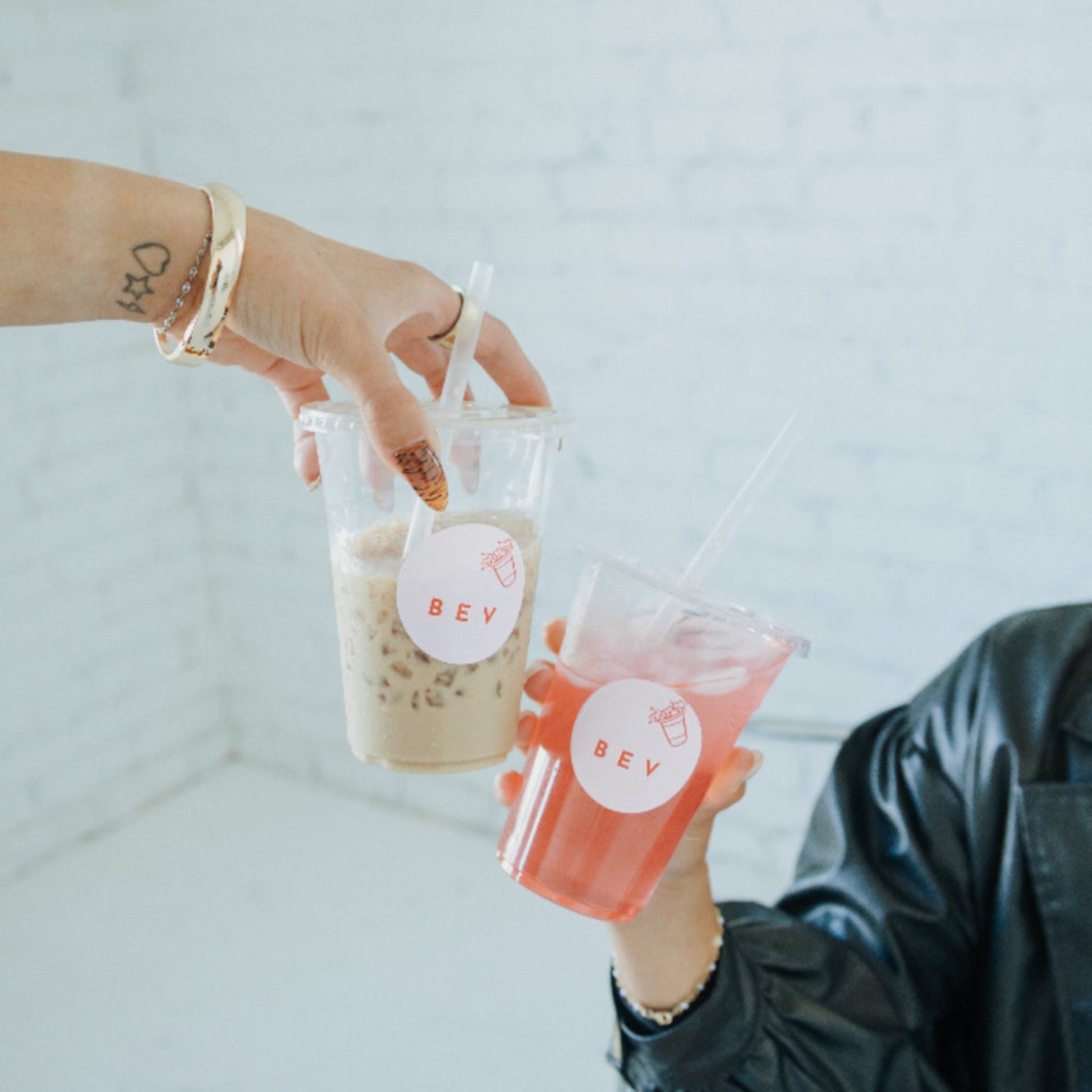 Two hands holding drinks with 'BEV' labels against a light background